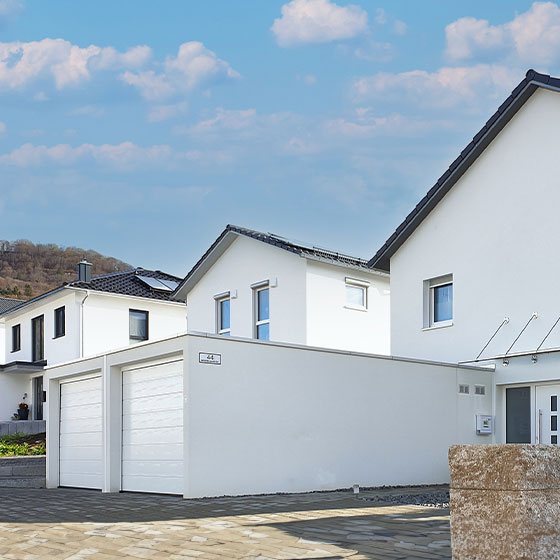 Das Bild zeigt eine außergewöhnlich lange Doppelgarage mit zwei getrennten Garagentoren. Die Rückseite der Garage ist direkt mit dem dahinterliegenden Wohnhaus verbunden, wodurch eine funktionale und platzsparende Architektur entsteht