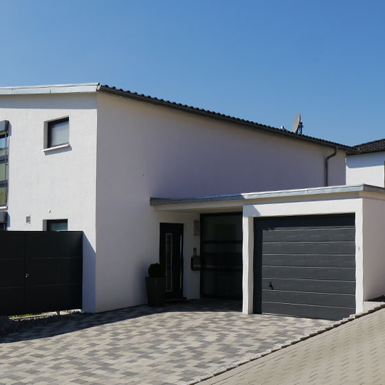 Das Bild zeigt eine Einzelgarage des Typs Profil Parto, die direkt mit dem Wohnhaus verbunden ist. Die Garage verfügt über ein dunkles Tor und präsentiert sich als klassischer Garagenstil, der sich harmonisch in die Hausarchitektur einfügt.