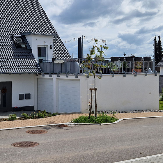 Doppelgarage dient gleichzeitig als Terrasse - Das Bild zeigt eine an das dazugehörige Haus angebaute Doppelgarage. Vor der Garage verläuft ein Gehweg. Auf dem Dach der Garage befindet sich eine Terrasse, die mit Partylichtern dekoriert ist. Eine Balkontür verbindet die Terrasse direkt mit dem Haus.