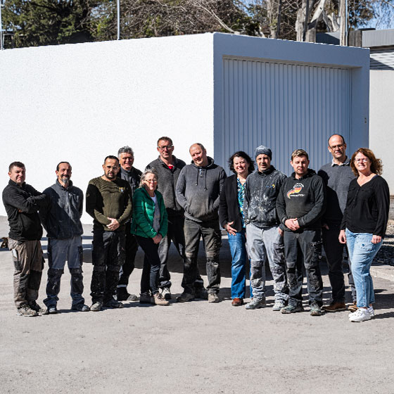 Wie wir zu dem Unternehmen wurden, das wir heute sind. Das Bild zeigt ein Gruppenbild der Firma IBK Villingen. Im Hintergrund ist eine große weiße Garage zu sehen.