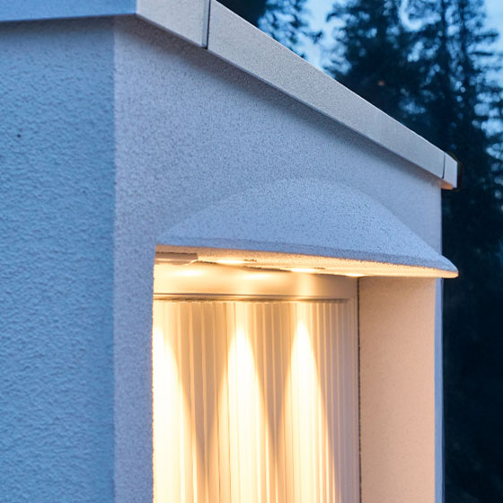 Das Bild zeigt eine Garage des Profils Vela. Das Garagentor ist in weiß und im oberen Bogen sind Lampen integriert, die eine indirekte Beleuchtung der Garagenfront ermöglichen. Die schwungvolle Form macht die Garagen zu einem dynamischen Blickfang.