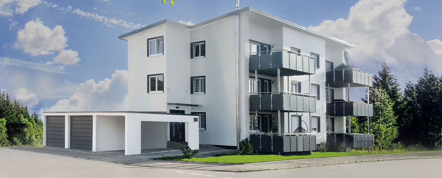 Das Bild zeigt ein weiß gestrichenes Mehrfamilienhaus mit sechs Balkonen auf der Frontseite, die alle in einem modernen Anthrazitton gehalten sind. Rechts neben dem Gebäude befinden sich zwei aneinandergereihte Garagen sowie ein Carport – ebenfalls direkt miteinander verbunden. Die Gesamtkomposition wirkt funktional und aufeinander abgestimmt