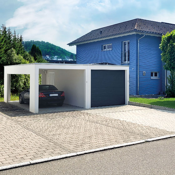 Das Bild zeigt eine moderne weiße Garage mit dunklem Tor, an die ein ebenfalls weißer Carport angebaut ist. Unter dem Carport steht ein schwarzes Mercedes Coupé. Rechts angrenzend befindet sich ein auffälliges blaues Wohnhaus mit Giebeldach, das vollständig mit blau gestrichenem Holz verkleidet ist. Vor dem Hauseingang steht eine farblich passende blaue Bank.