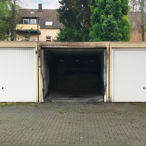 Drei Garagen, die mittlere ohne Tor und durch einen Brand stark beschädigt – Symbolbild für Brandschutz bei E-Autos.